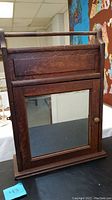 Front view of antique wooden medicine cabinet with framed mirror door and towel rod on top.