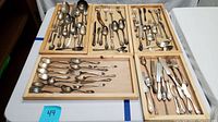 Wide view of multiple wooden trays containing a variety of silverplate flatware including forks, spoons, and knives arranged loosely.