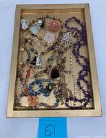 Image showing collection of assorted costume jewelry in wooden tray including necklaces, pendants, and earrings.
