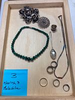 Jewelry set arrayed in wooden tray including brooch, malachite necklace, rings, colorful beaded necklace, and teaspoon