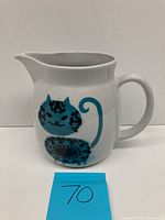 Front view of the white ceramic pitcher showing the blue and black stylized cat design on one side.