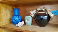 Shelf displaying a blue art pottery vase, a green sparrow-shaped vase, a small pink bird-shaped incense burner, and a dark brown covered pottery jar with rope handle.