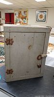 Photo of white painted wooden country kitchen cupboard with decorative metal hinges and small knob.