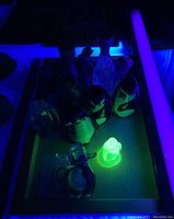 Figurines under UV light showing glowing yellow Vaseline glass penguin, with other glass and ceramic animal figurines on wooden tray