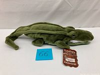 Full side view of green plush crocodile puppet with tag and zipper on mouth