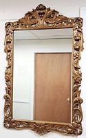 Full view of the vintage gilt ornate wall mirror hanging on a wall showing overall condition and dimensions in relation to the door beside it.