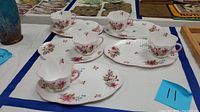 Four porcelain luncheon sets each with a cup and matching plate with pink floral decoration on a white base with scalloped edges.