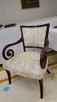 Front angle showing upholstered seat and backrest with floral pattern and dark wood frame with scroll arms.