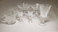 Eight Waterford crystal glasses in Lismore pattern arranged on a flat surface including various types and sizes of glasses.
