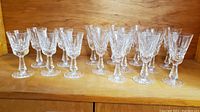 Wide view showing 18 Waterford Crystal sherry glasses in Lismore pattern arranged on wooden surface.