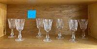 Six vintage Waterford cut crystal cordial stem glasses arranged on a wooden shelf, showing full collection.