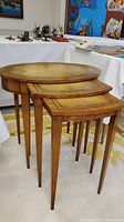 Three vintage Weinmann heirloom nesting tables with leather tops and tapered wooden legs, shown nested together on a carpeted floor near other furniture and artwork.