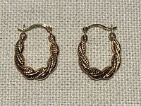 Shows the pair of twisted 10K gold hoops with textured detail on fabric background