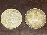 Two Chinese silver coins side by side on dark wood surface, showing obverse and reverse details.