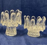 Two clear crystal Kosta Boda sunflower themed candleholders with petal arms, displayed on blue fabric background