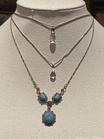 Three sterling silver necklaces displayed on a mannequin bust showing their pendants and chains.