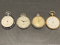 Four vintage pocket watches laid in a row, showing front dial views and overall condition.
