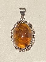 Front view of oval amber pendant in silver setting with decorative border.