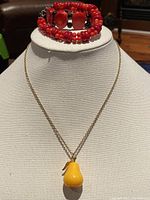 Amber pear pendant necklace displayed on beige bust stand with two red coral beaded bracelets placed on top of the stand.