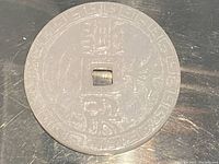 Front side of carved jade coin pendant showing detailed engraved Chinese characters and motifs with central square hole.