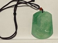 Front view of rectangular green jade pendant on black cord with amber bead near knot for necklace suspension.