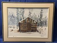Full view of the framed oil painting depicting a wooden cabin in snow with pine trees in background.