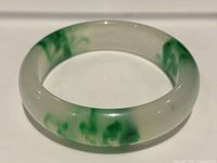 Close-up image showing a section of the jade bangle highlighting the translucent base and green mottled areas under smooth polished finish.