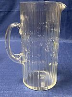 Clear glass pitcher showing ribbed vertical lines with bubbles and a handle