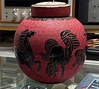 Side view of the red ginger jar showing black embossed horses and textured swirling background.
