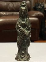 Front view of the bronze standing woman sculpture showing detailed facial features, necklace, and draped garments.
