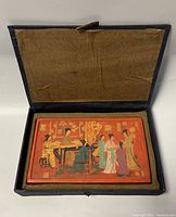 Open blue cloth-covered box with lined interior holding cinnabar lacquer plaque