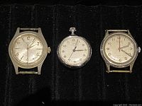 Three vintage windup watches varying in size and style laid flat on black background.