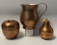 Front view of three copperware items: apple and pear containers with lids and a pitcher