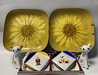 Two Bovano square cloisonné enamel plates with yellow sunflower design alongside two white ceramic salt and pepper shakers with blue accents and two Ando small square enamel plates in box
