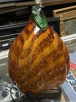 Close-up front view of the amber and brown blown glass gourd sculpture with green stem showing swirling pattern and ribbed texture.