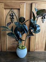 Full view of faux plant with multiple dark green leaves in white ceramic pot