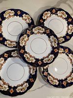 Top view of five vintage Royal Albert Crown China plates arranged in a fan shape, showcasing the navy blue border with floral and gold decorative elements and white center.