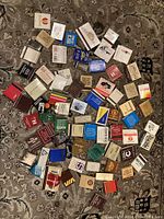 Top down view of 73 matchbooks laid out on a patterned carpet, showing various colors and logos representing vintage advertising on matchbooks.