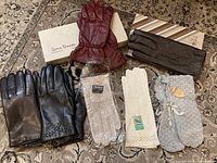 Seven pairs of gloves and mittens displayed on a patterned rug, with some pairs inside or near their vintage boxes.