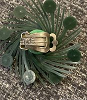Close-up showing green plastic clip-on earring with clip stamped Made in Western Germany