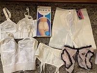 Lot of six vintage lingerie pieces laid out including bras, panty girdle, garter belt, and panties