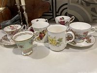 View of all tea cups, saucers and mugs displayed on a table showing different floral patterns and styles.