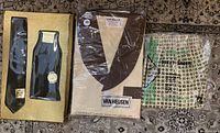Photo showing the full lot of three original packaged items: a Van Heusen pyjama set (brown and cream), a black tie in nylon packaging, and boxer shorts in patterned packaging.