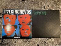 Shows front covers of both Talking Heads vinyl albums, 'Remain in Light' with stylized orange faces on a blue background and 'Fear of Music' with black textured diamond plate cover and green title text.