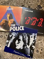 Three vinyl albums by The Police displayed on a carpet: Reggatta De Blanc, Ghost in the Machine, and Zenyatta Mondatta.