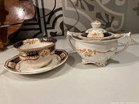 Photo showing the cup, saucer, and lidded creamer on a countertop with clear view of floral and gold details, and cobalt blue decoration.