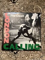 Front cover of 'London Calling' vinyl album showing band member in black and white image with bold pink and green text.