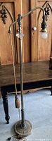 Full view of vintage floor lamp showing curved arm, tassel pull, round ornate base, and single light socket with bulb.