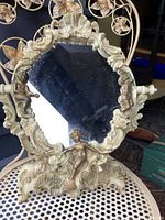 Front view of the resin swivel mirror showing ornate frame with two cherubs and shell motif at the top and bottom, mirror surface reflecting surroundings.