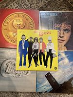Five vintage vinyl album covers arranged in a pile: Earth Wind & Fire Vol. 1, David Essex 'Rock On', The B-52's self-titled with yellow cover, Chicago with silver logo cover, Three Dog Night 'Naturally' with scenic sky and ocean cover.